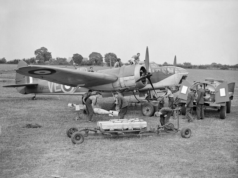 Armourers loading bombs onto a Bristol Blenheim Mk IV of No. 110 Squadron on the grass at Wattisham, with a bomb trolley in the foreground.