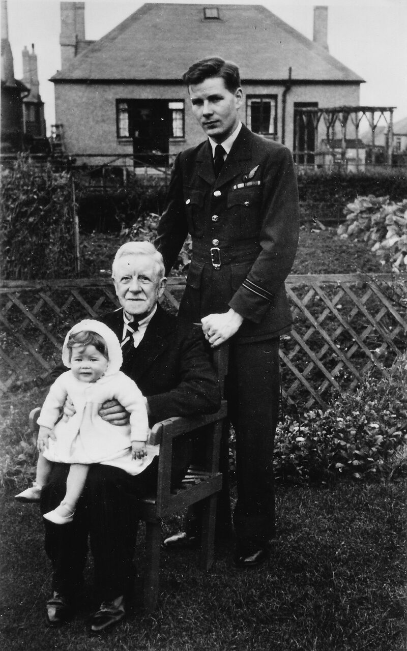 E G White in RAF officer’s uniform standing behind his seated grandfather, who holds White’s infant daughter, in a garden in Edinburgh, October 1946.